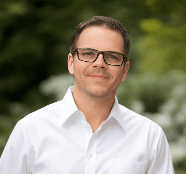 A man in glasses and white shirt smiling for the camera.