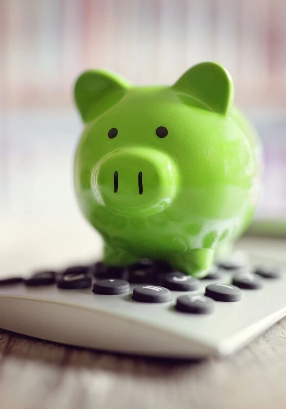 A green piggy bank sitting on top of a calculator.